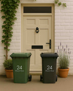 Two trash bins, one green and one black, with the number 24 on a white door background.