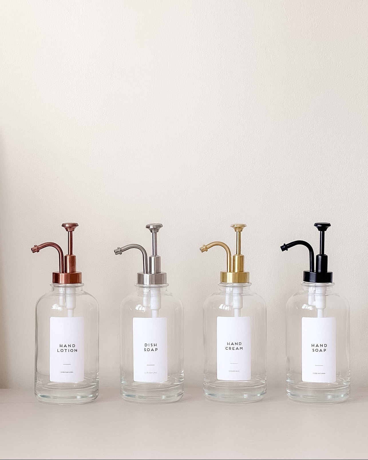 Four glass bottles with metal pumps on a light background