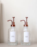 Two glass bottles with copper pumps on a neutral background