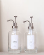 Two glass dispensers with pump tops labeled 'Hand Lotion' and 'Dish Soap' on a neutral background.